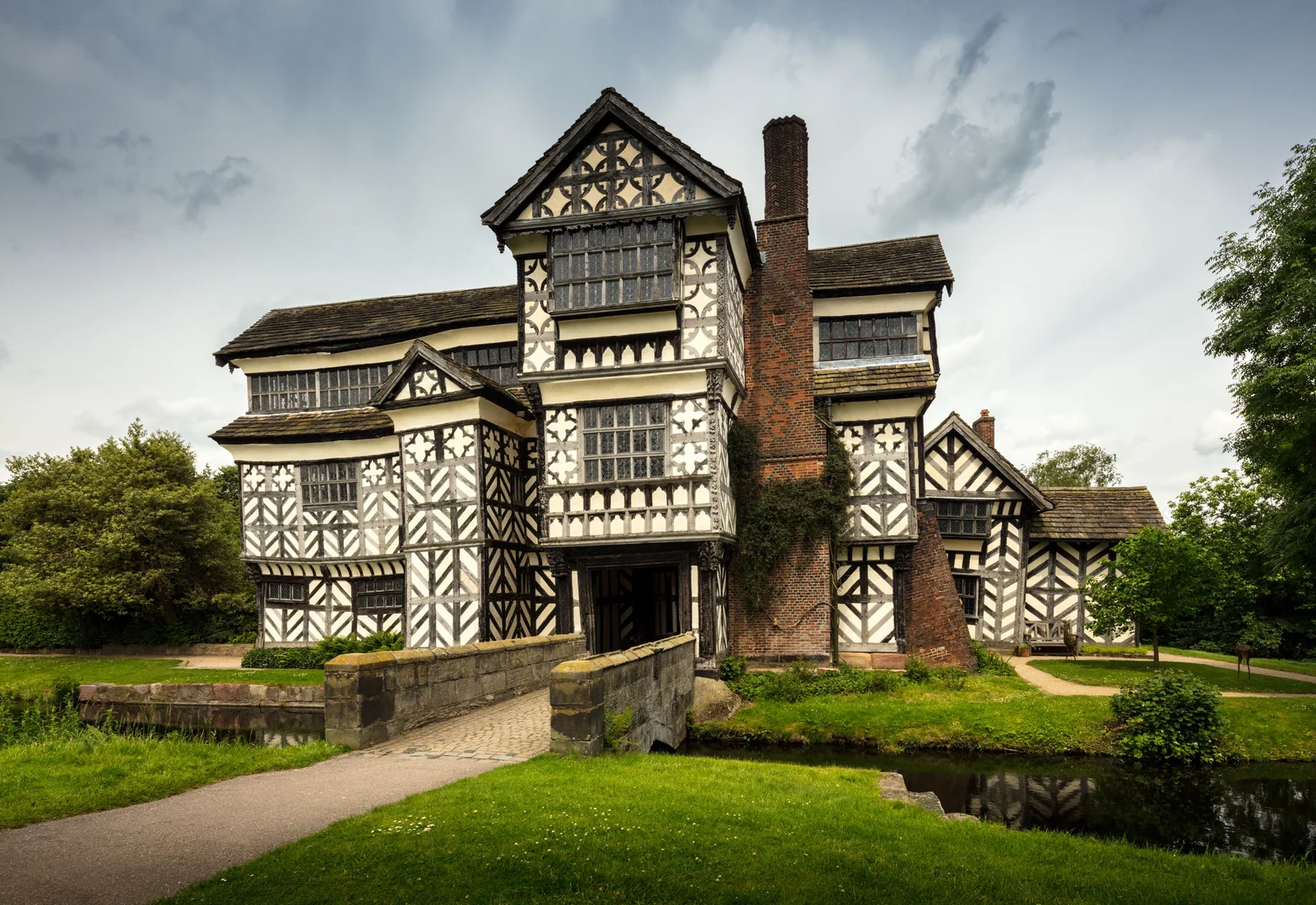 A timber-framed historic house surrounded by mature trees.