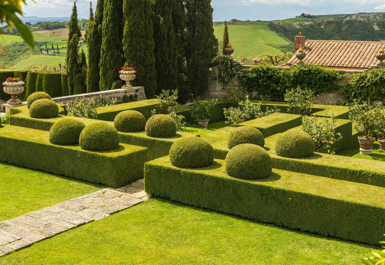 A formal garden composed of clipped hedges, trees, and distant hills.